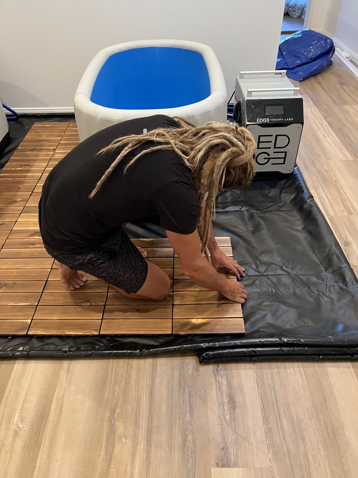 Interlocking wood floor tiles being laid around a cold plunge tub during build-out