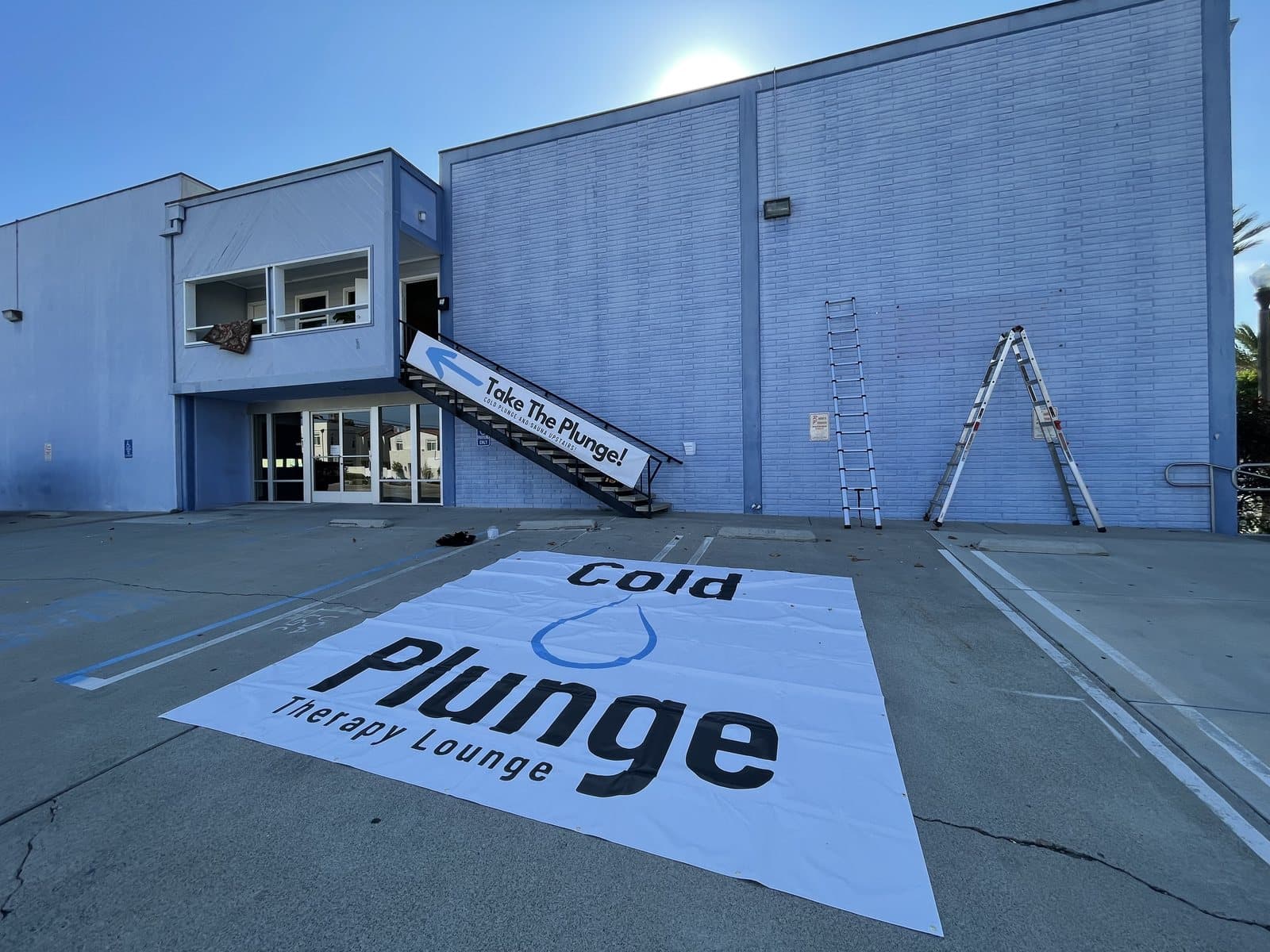 A large storefront sign laid flat on the parking lot pavement before installation, banner hung on the stairs above